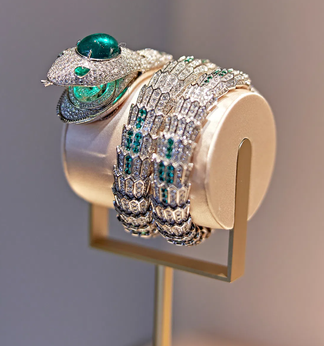A coiled serpent high-jewelry bracelet set with diamonds and emeralds, displayed on a cream satin roll