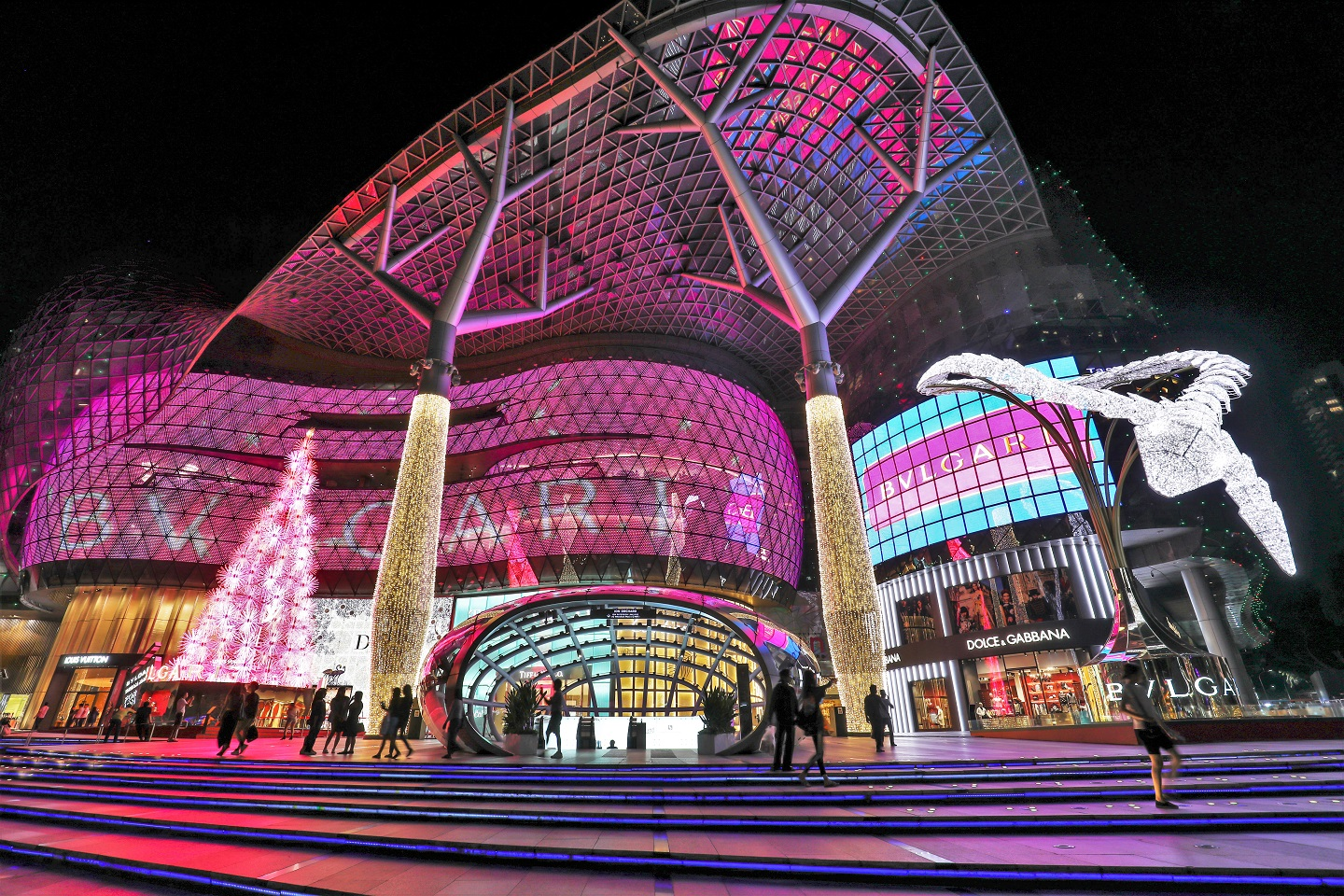 ION Orchard in Singapore lit in pink for the BVLGARI Serpenti Light Up, with golden light-wrapped columns, a glowing white tree and a white illuminated snake sculpture